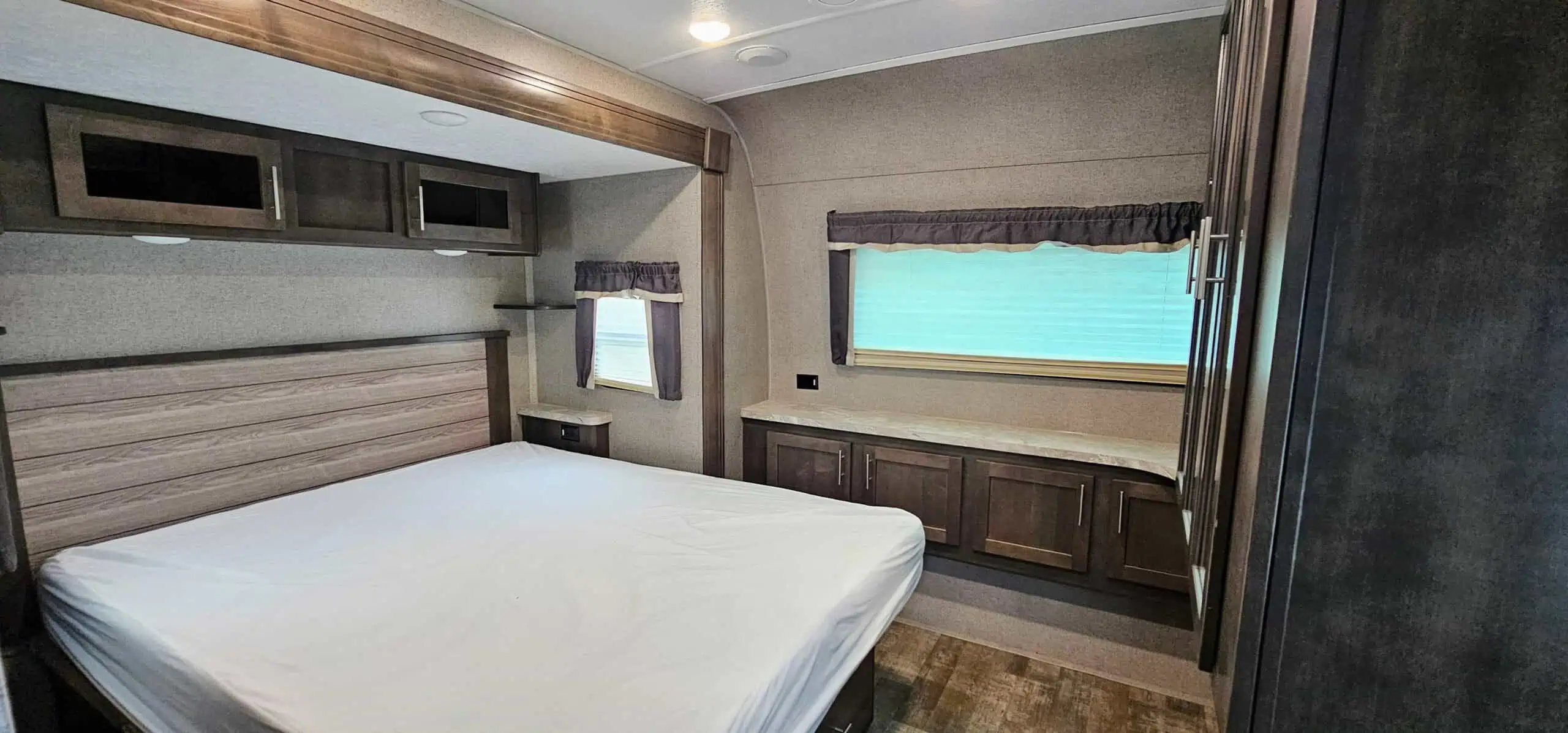 Interior of modern RV bedroom with bed and cabinets.