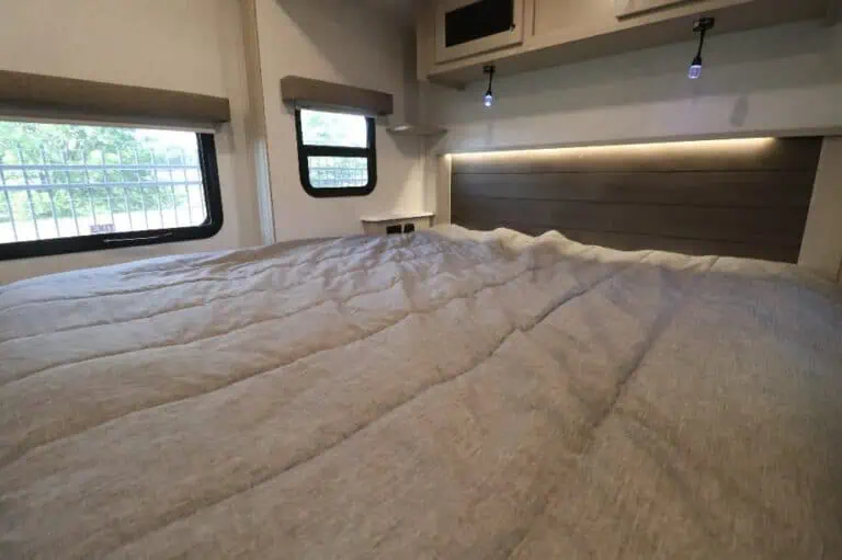 Cozy bed in RV interior with windows.