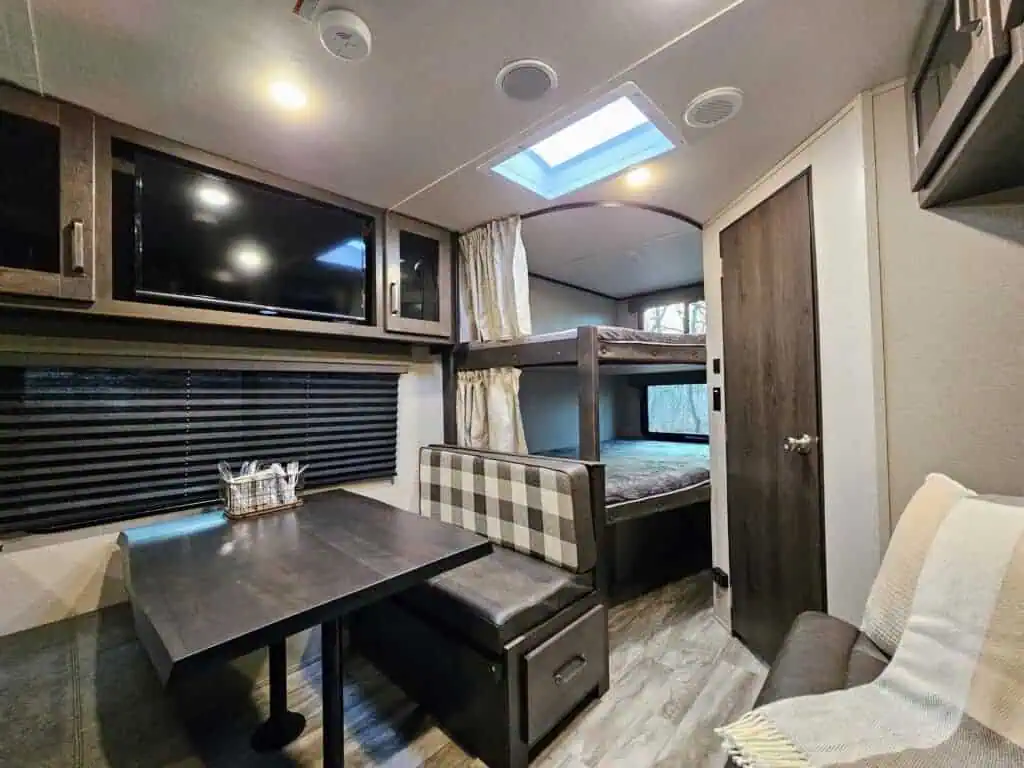 Modern RV interior with bunk beds and dining area.